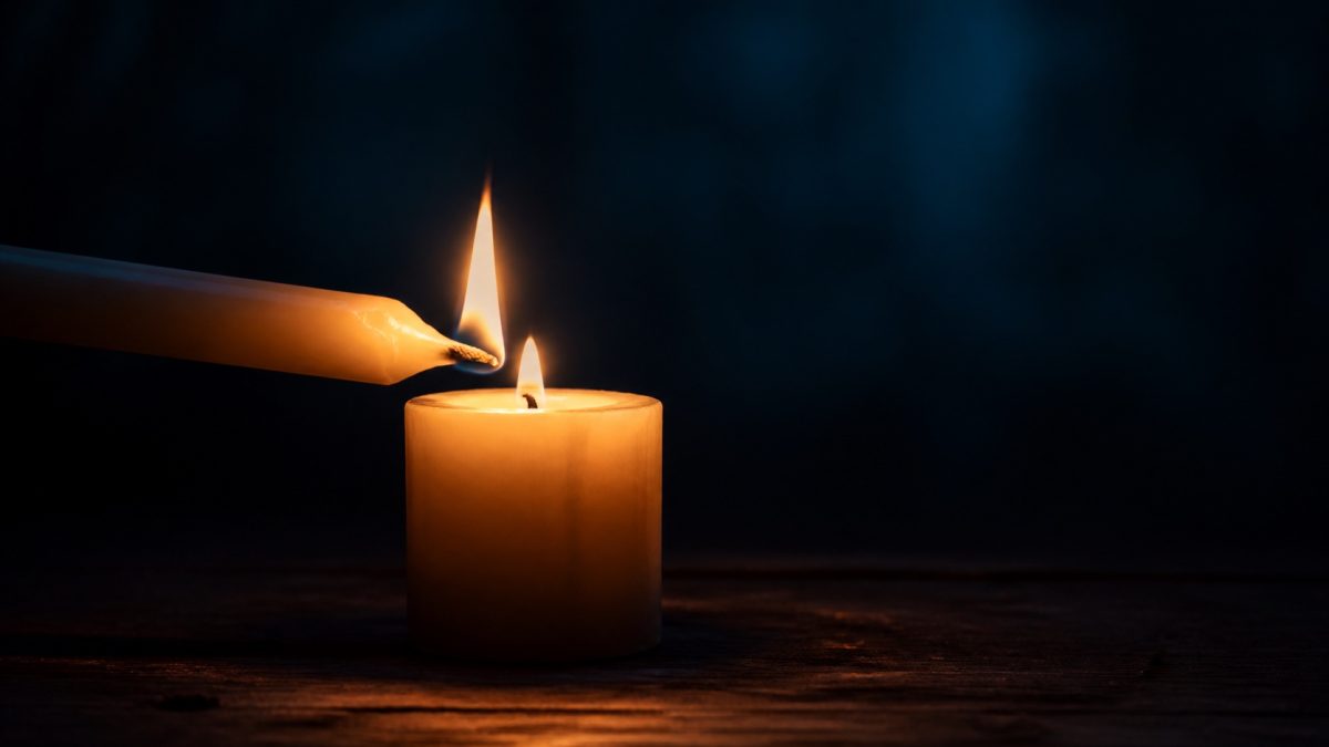 Two candles sharing a flame in the darkness, symbolising constructive action and hope.